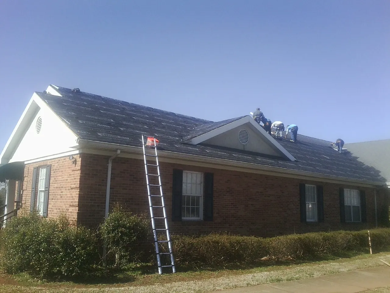 Crew tearing shingles off a brick ranch roof with a ladder set — Metal Roof Repair work by our crew in Orwigsburg