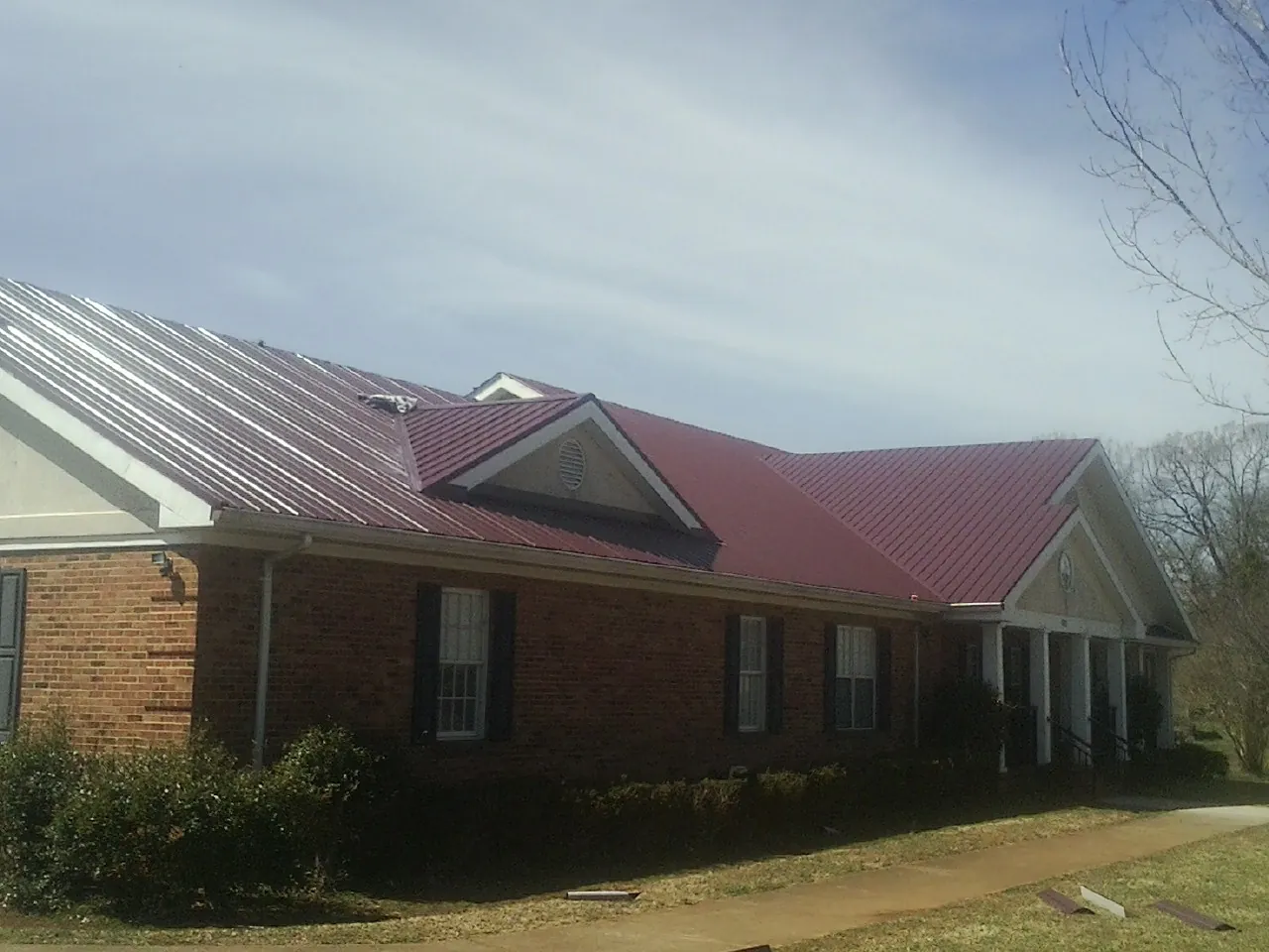Red metal roof with gabled entries on a long brick building, from a Hail Damage Roof Repair job in Orwigsburg