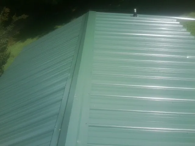New green metal panels meeting at the ridge of a roof — Flat Roof Repair work by our crew in Orwigsburg