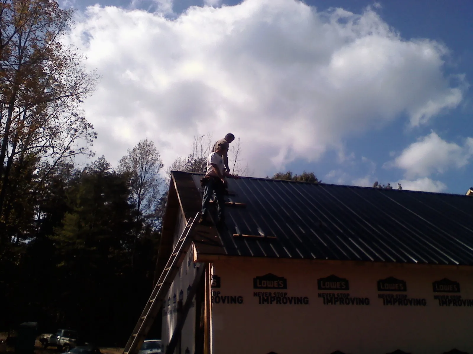 Roofer fastening dark metal panels high against a cloudy sky, from a Roof Inspection job in Orwigsburg