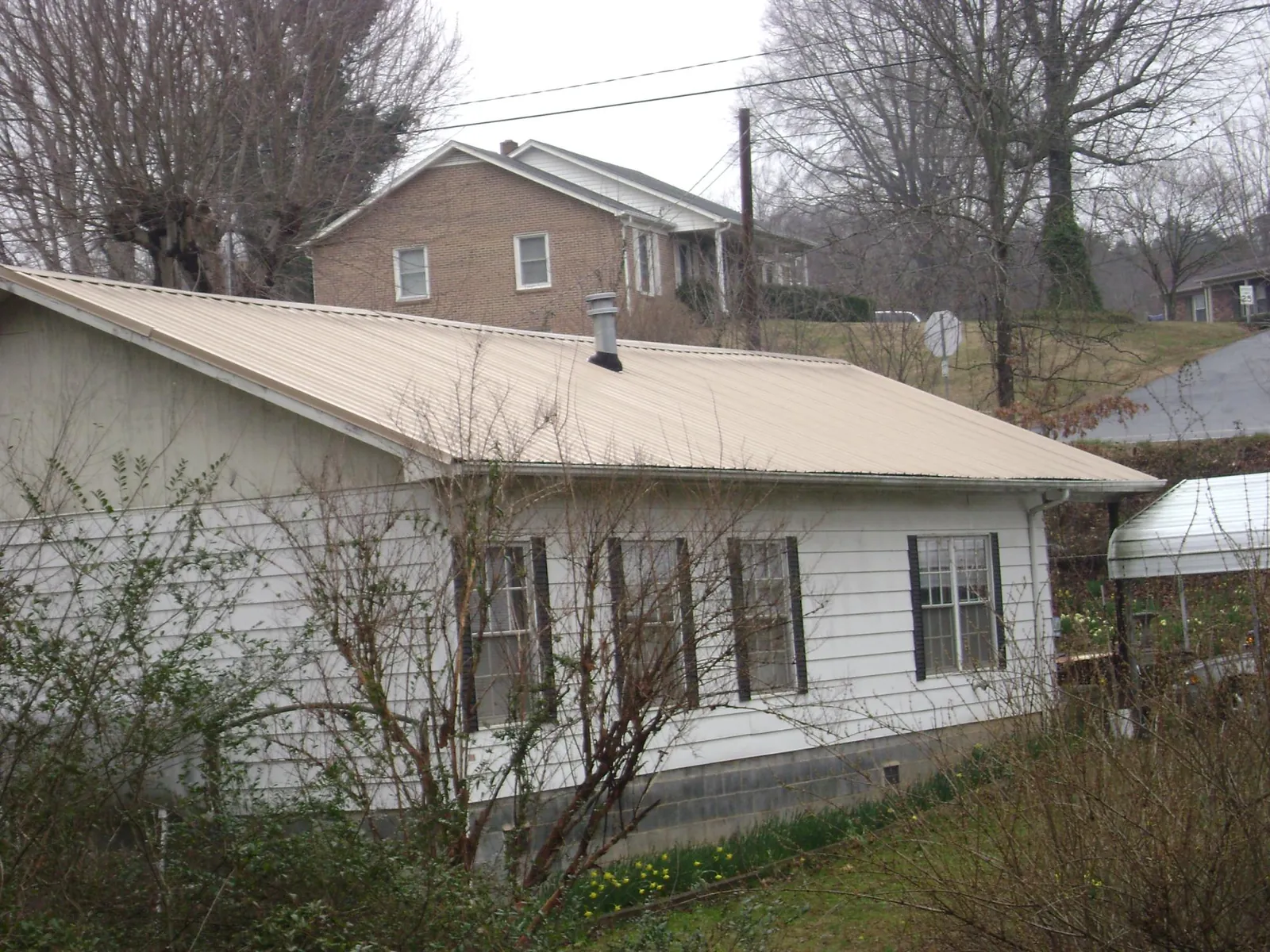 Tan metal roof on a white sided house set into a hillside — Commercial Roofing by Roofing Brothers in Orwigsburg